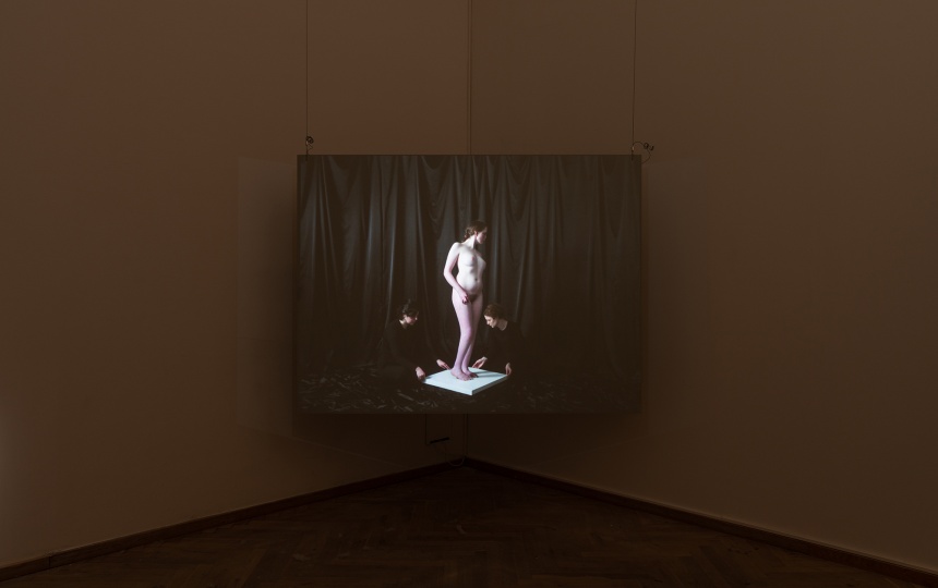 Installationsfoto af Luna Emilie Printz Scales' afgangsværk Eyelids (skærm med nøgen kvinde på plint som drejes af to personer)