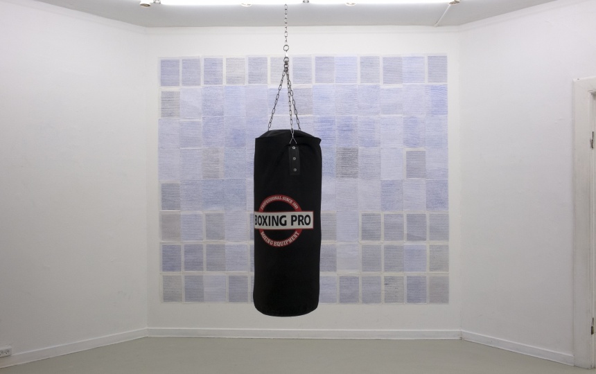 Kunstværk der hænger ned fra loftet foran et andet værk på væggen i Udstillingsstedet Q